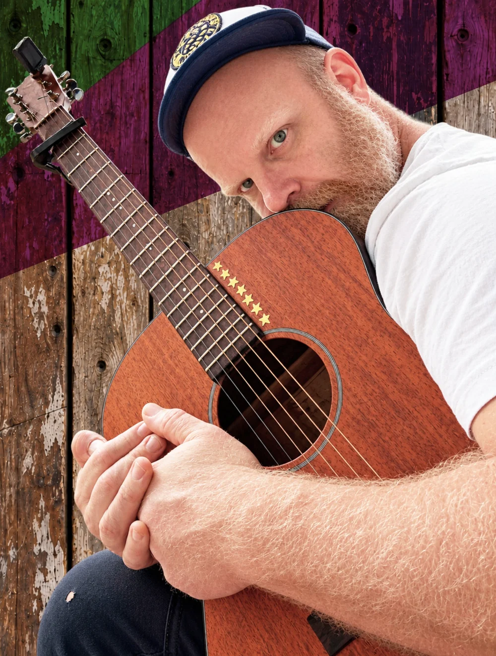 Jay Bones leaning against his acoustic guitar against a painted wooden background
